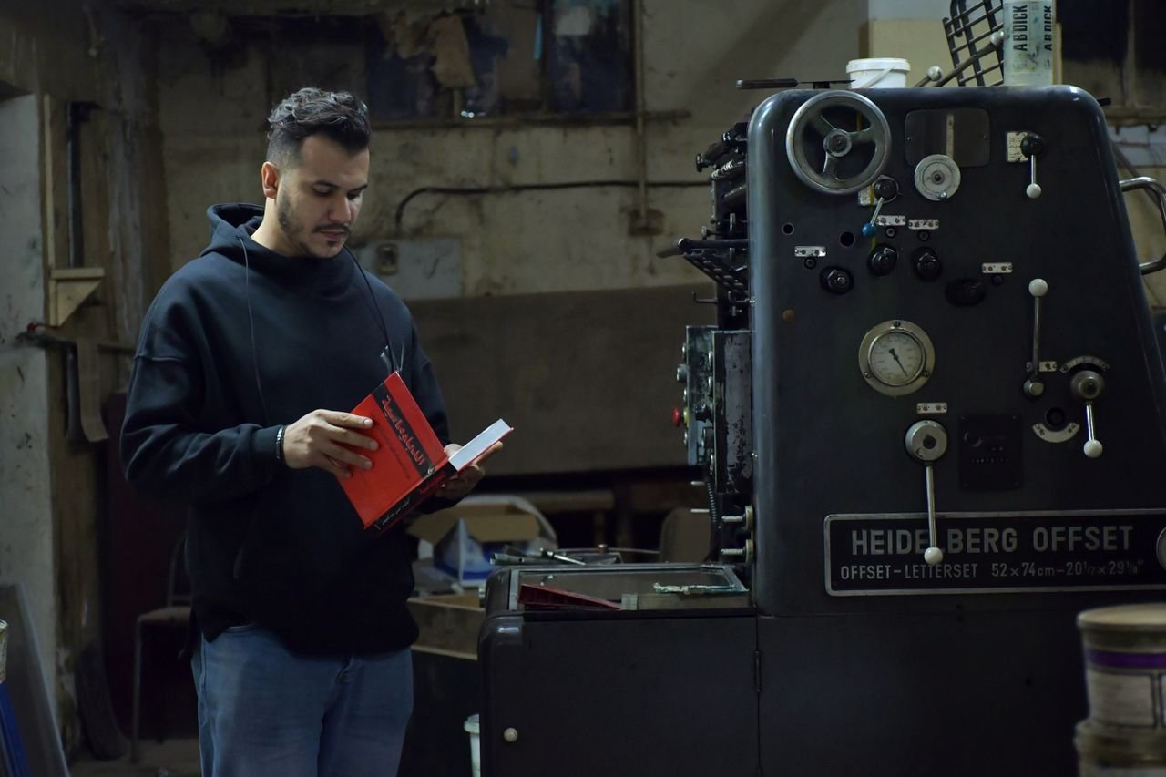 Services A man in a black hoodie reads by an industrial printing machine in Benghazi, Libya.