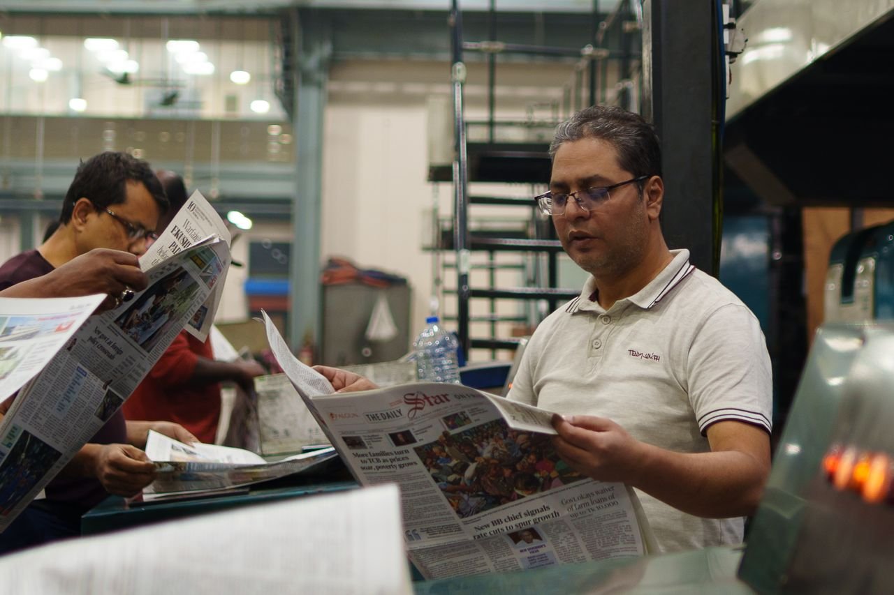 The Art of Drawing Readers In: Your attractive post title goes here Workers at a newspaper printing press reading freshly printed copies. Focus on a man holding a newspaper.