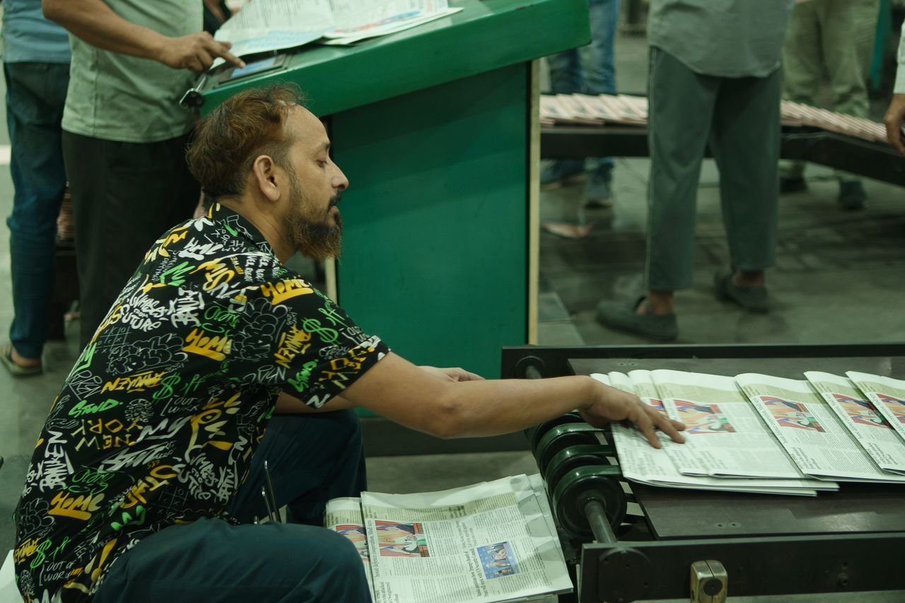 Services Man sorting newspapers on a conveyor belt in a busy printing press environment.