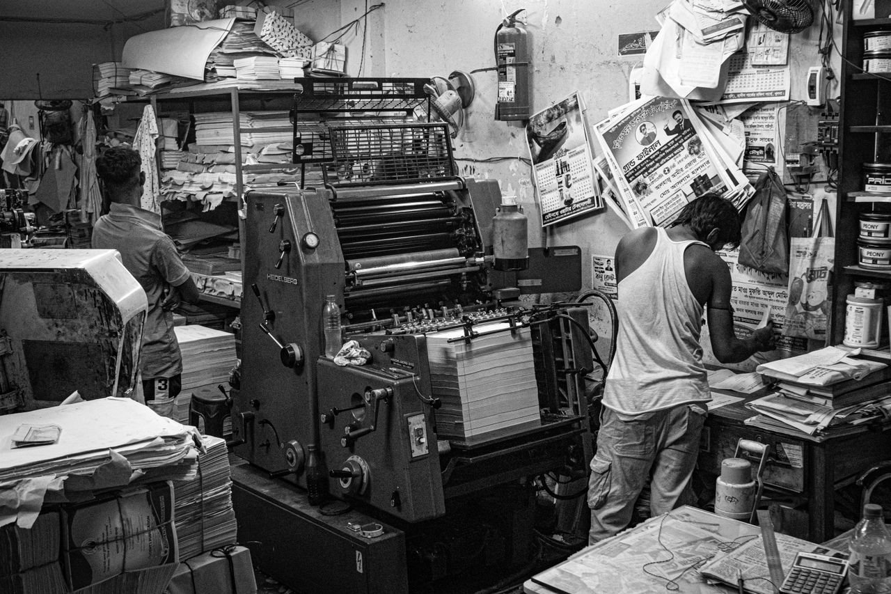 Services Black and white image of a bustling print shop with workers operating a printing press.
