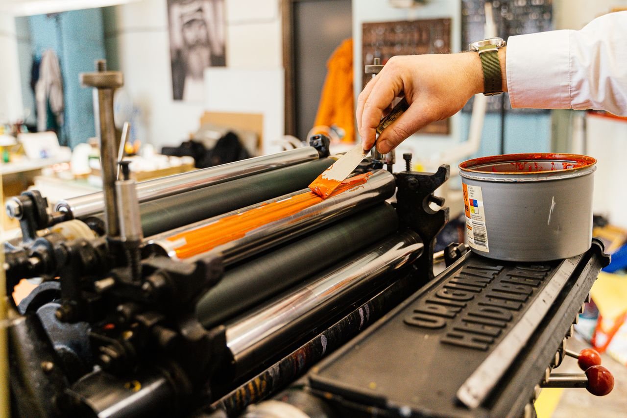 Crafting Captivating Headlines: Your awesome post title goes here A detailed view of a hand applying orange ink to a vintage printing press roller indoors.